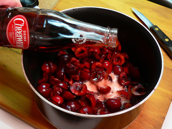 Pour in the two bottles of Cheerwine. It fizzes a lot because of the carbonation. We're using two bottles because we want to fully cook the cherries in the cola and let the cola reduce down. It's not going to completely thicken up as it cooks, but you need to let it cook until you have just a little more than a cup of liquid in the cherries. As the cola cooks down, the flavors and the sugar of the Cheerwine will intensify. Please note that the recipe will not work as well with diet Cheerwine. Spring for the regular stuff.