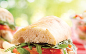Chicken pesto and tomato sandwich on a picnic table