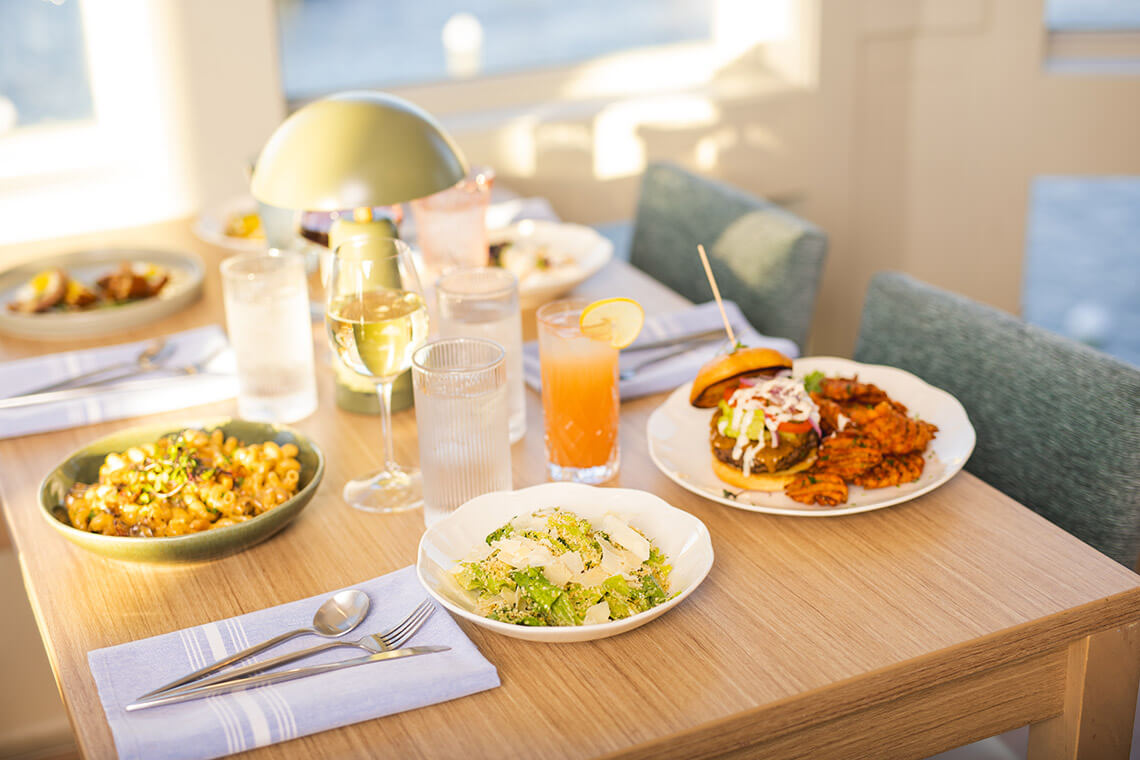 Pasta, salad, and burger on a table with drinks at Salt & Cypress